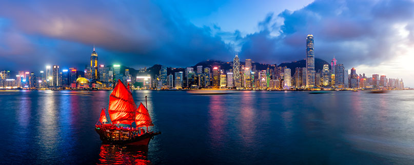 Panorama of Hong Kong City skyline with tourist sailboat at night. View from across Victoria Harbor HongKong.