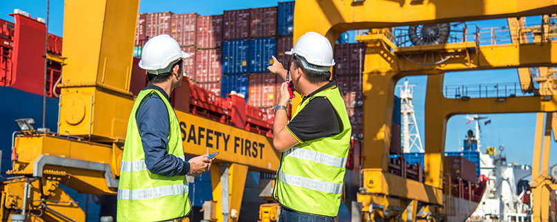 worker working with radio transceiver for controlling crane to loading container box to container ship in port shipping containers. logistics, sea transportation and logistics business concept