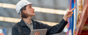 Woman wearing hard hat pointing to a shipping box on a shelf.