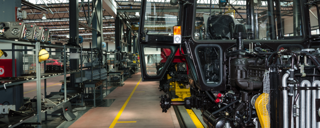 A tractor chassis sits on a factory floor surrounded by shelving and supplies