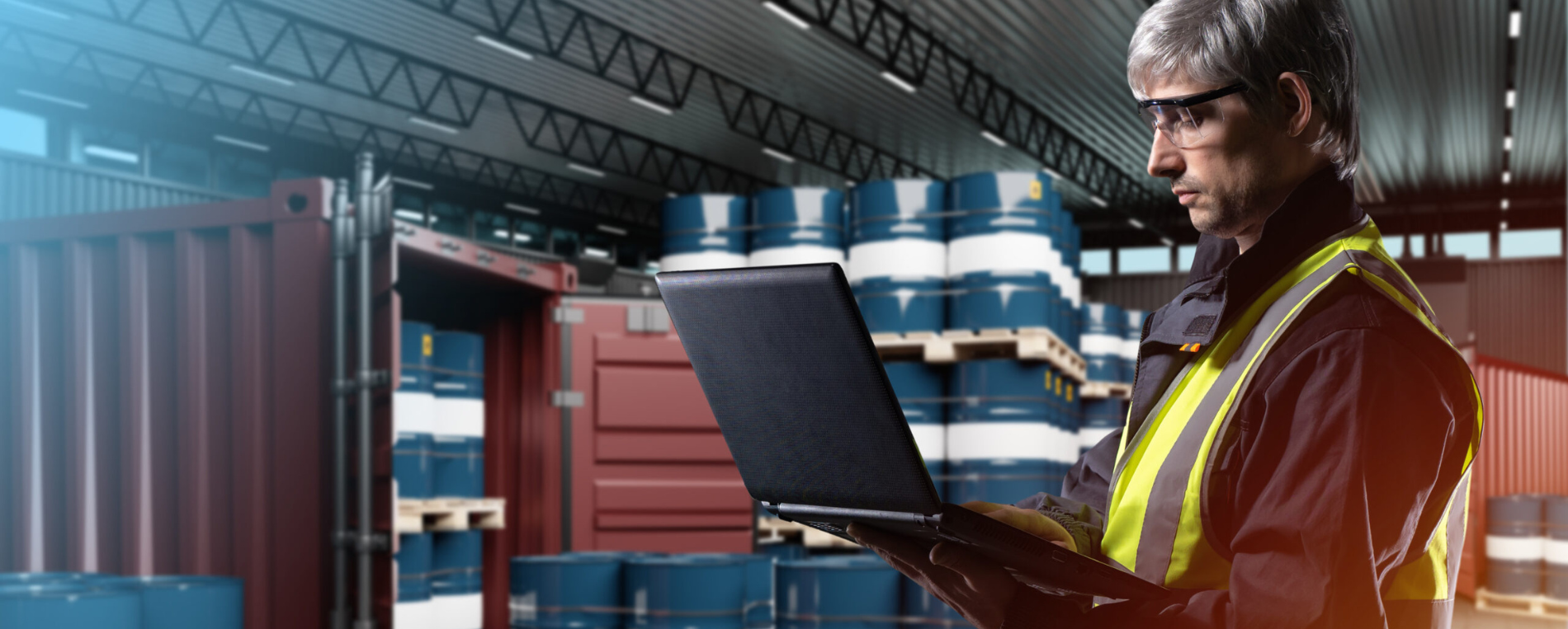 a logistics manager holds a computer in a warehouse next to a cargo container