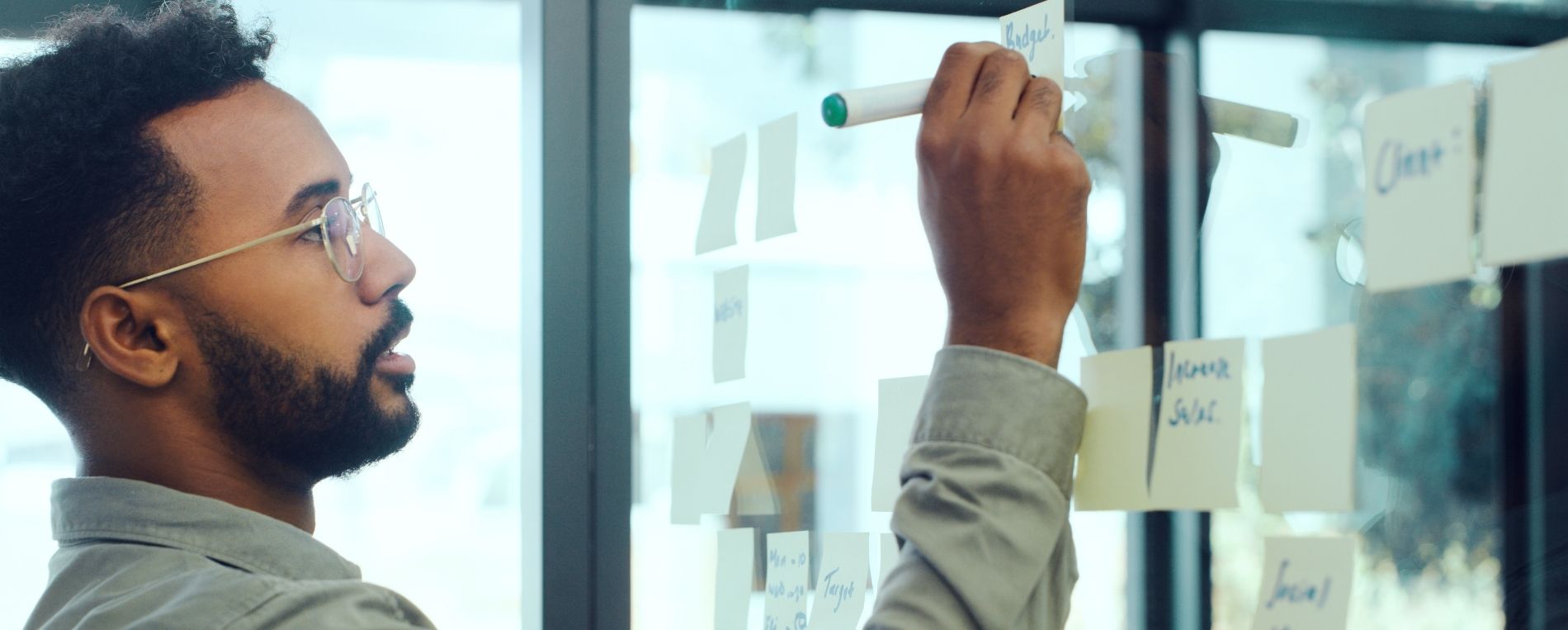 A person in a collared shirt writes on a clear white board